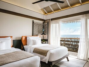 Une chambre d’hôtel avec deux lits, un ventilateur de plafond, une vue sur la mer et un balcon doté d’une balustrade en bois.