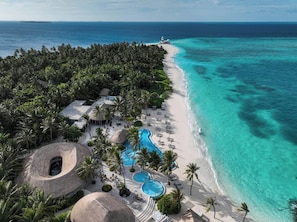 An aerial view of a resort with a beach, a pool area, and a lighthouse.