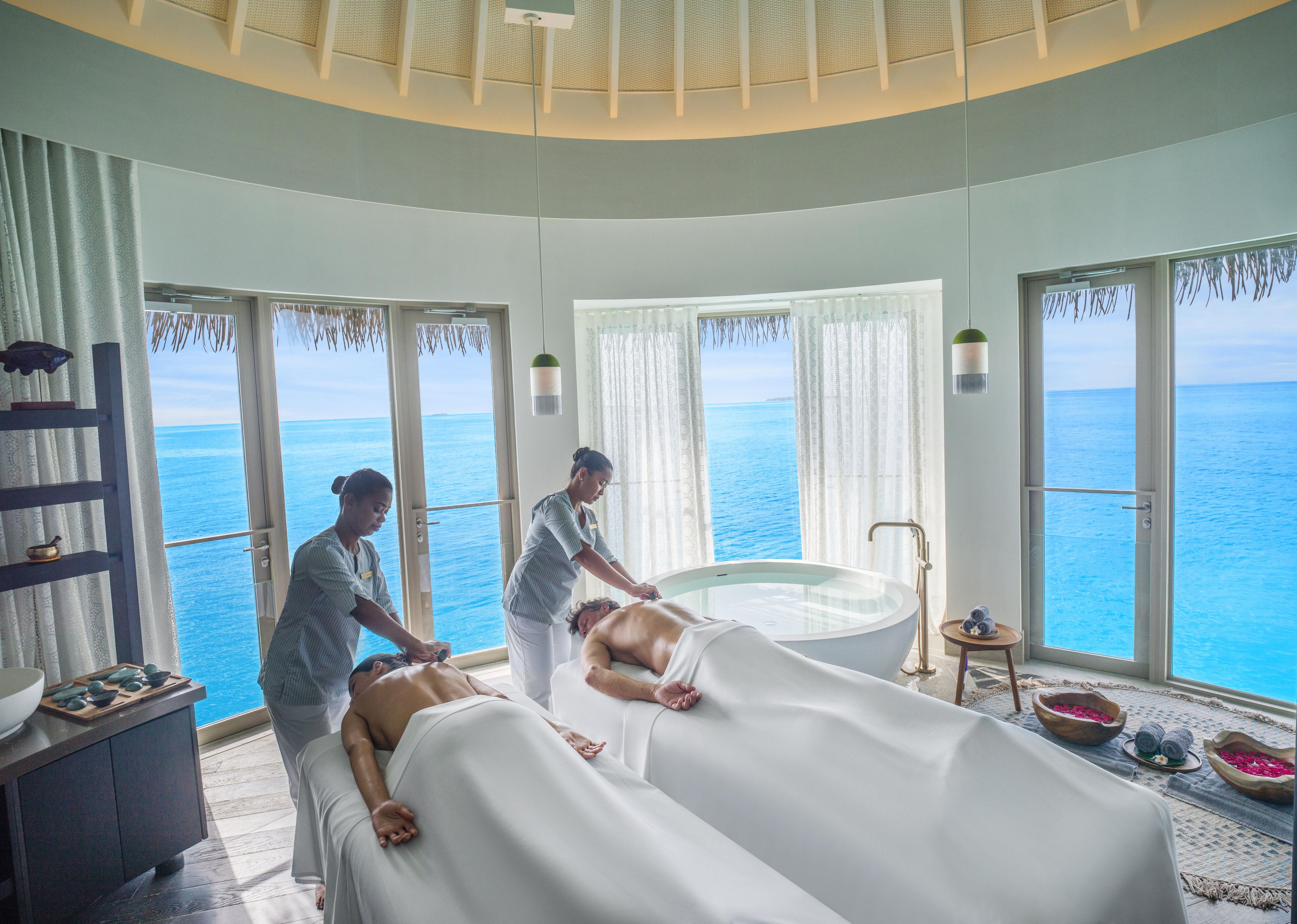 A spa room with a massage table, a bathtub, and a view of the ocean.