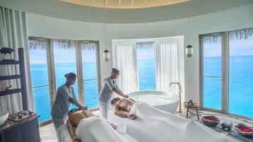 A spa room with a massage table, a bathtub, and a view of the ocean.