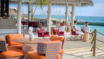 A resort deck with outdoor seating, a bar area, and a view of the ocean.