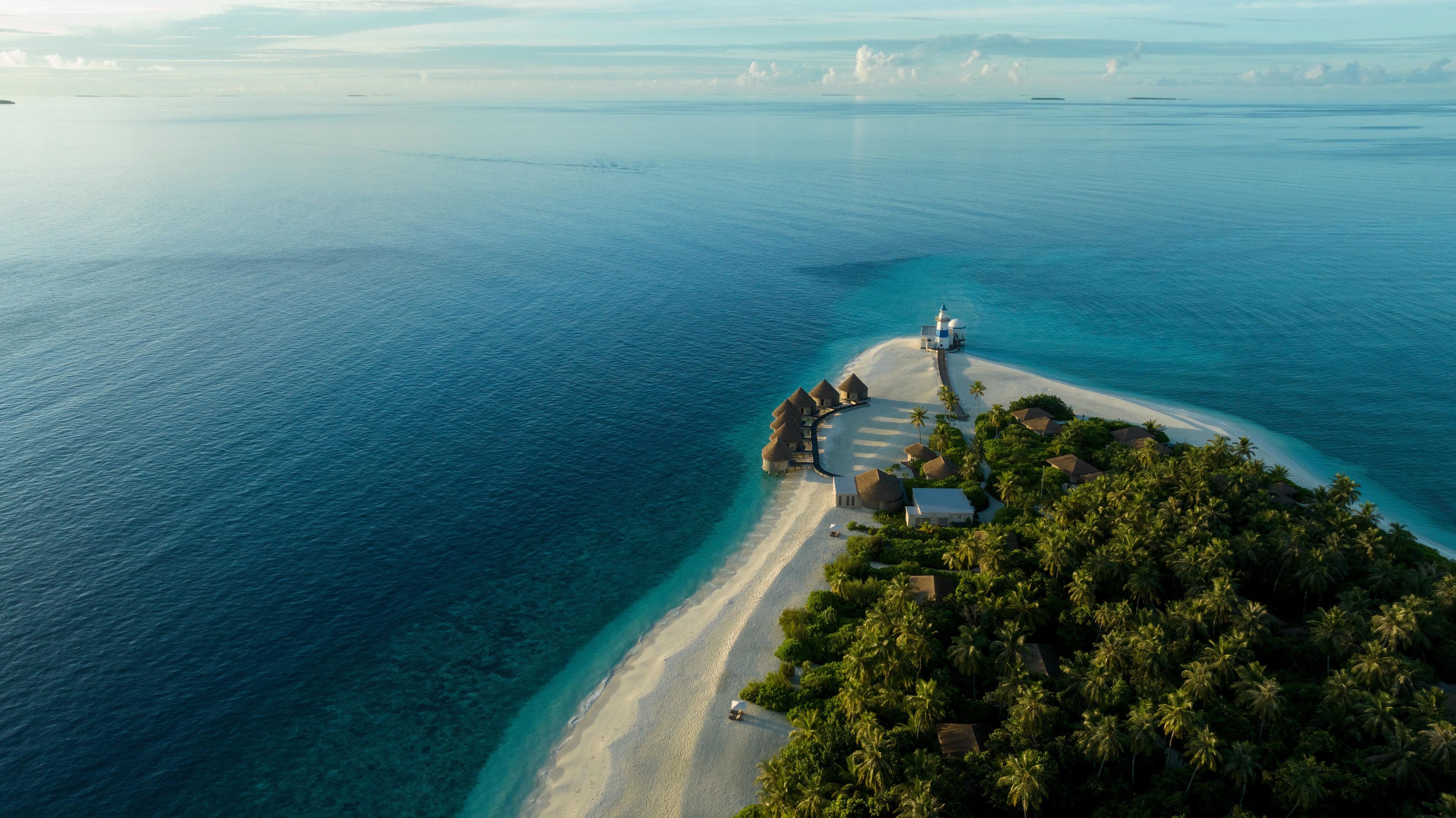 Ein Luftbild eines tropischen Inselresorts mit Bungalows über dem Wasser, einem Leuchtturm und einem Strand.