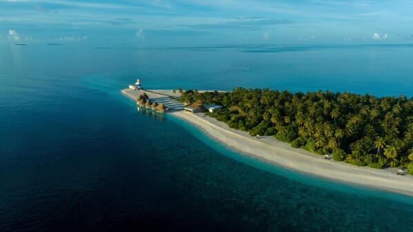 An aerial view of a tropical island with a beach, overwater bungalows, and a lighthouse.