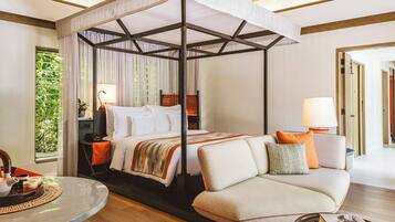 A modern hotel room with a four-poster bed, a sofa, a dining table, and a view of greenery outside.
