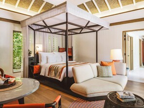 Ein modernes Hotelzimmer mit Himmelbett, einer Couch, einem Esstisch und Blick auf Grünfläche.