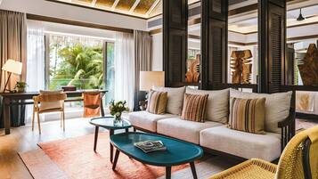 A modern living room with a sofa, coffee table, and chairs, large windows with a view of greenery, and a ceiling with a geometric pattern.