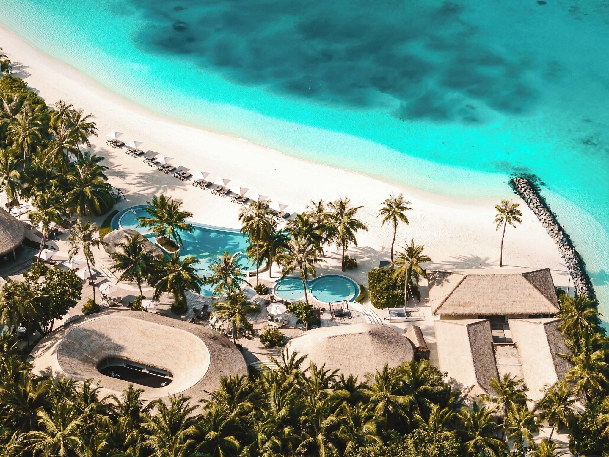 A resort with a beach, palm trees, and multiple swimming pools.