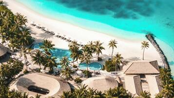 A resort with a beach, palm trees, and multiple swimming pools.