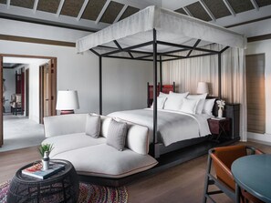 A modern hotel room with a four-poster canopy bed, a sofa, a small round table, and a chair. - Intercontinental Maldives Maamunagau Resort (Maamunagau Island)