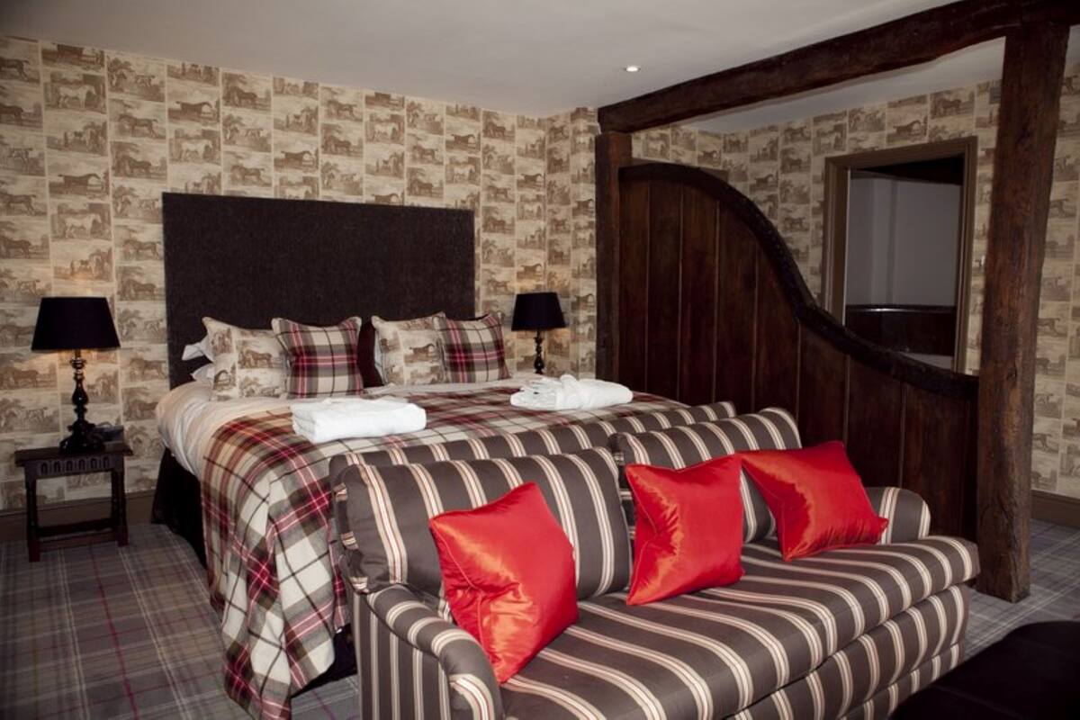 Un lit avec une tête de lit, une table de chevet avec une lampe, un banc avec des coussins et une porte en bois.