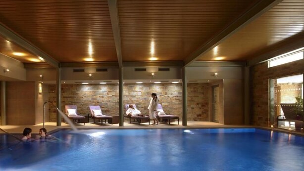 A swimming pool with lounge chairs, a person walking, and a stone wall. - The Greenway (Cheltenham)