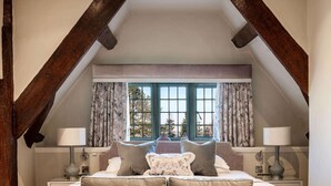 A bedroom with a loft-style ceiling, a bed with multiple pillows, a grey sofa, and a window with curtains. - The Greenway (Cheltenham)