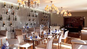 A restaurant with multiple tables, chairs, and a wall of wine bottles. - The Greenway (Cheltenham)