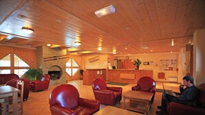 A cozy interior with wooden ceilings, red leather chairs, a fireplace, a reception desk, and a laptop on a table. - Lagrange Vacances Les Valmonts De Val Cenis (Val-Cenis)