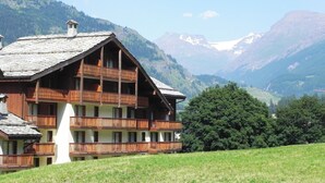 A wooden chalet with multiple balconies, set against a backdrop of mountains and clear skies. - Lagrange Vacances Les Valmonts De Val Cenis (Val-Cenis)