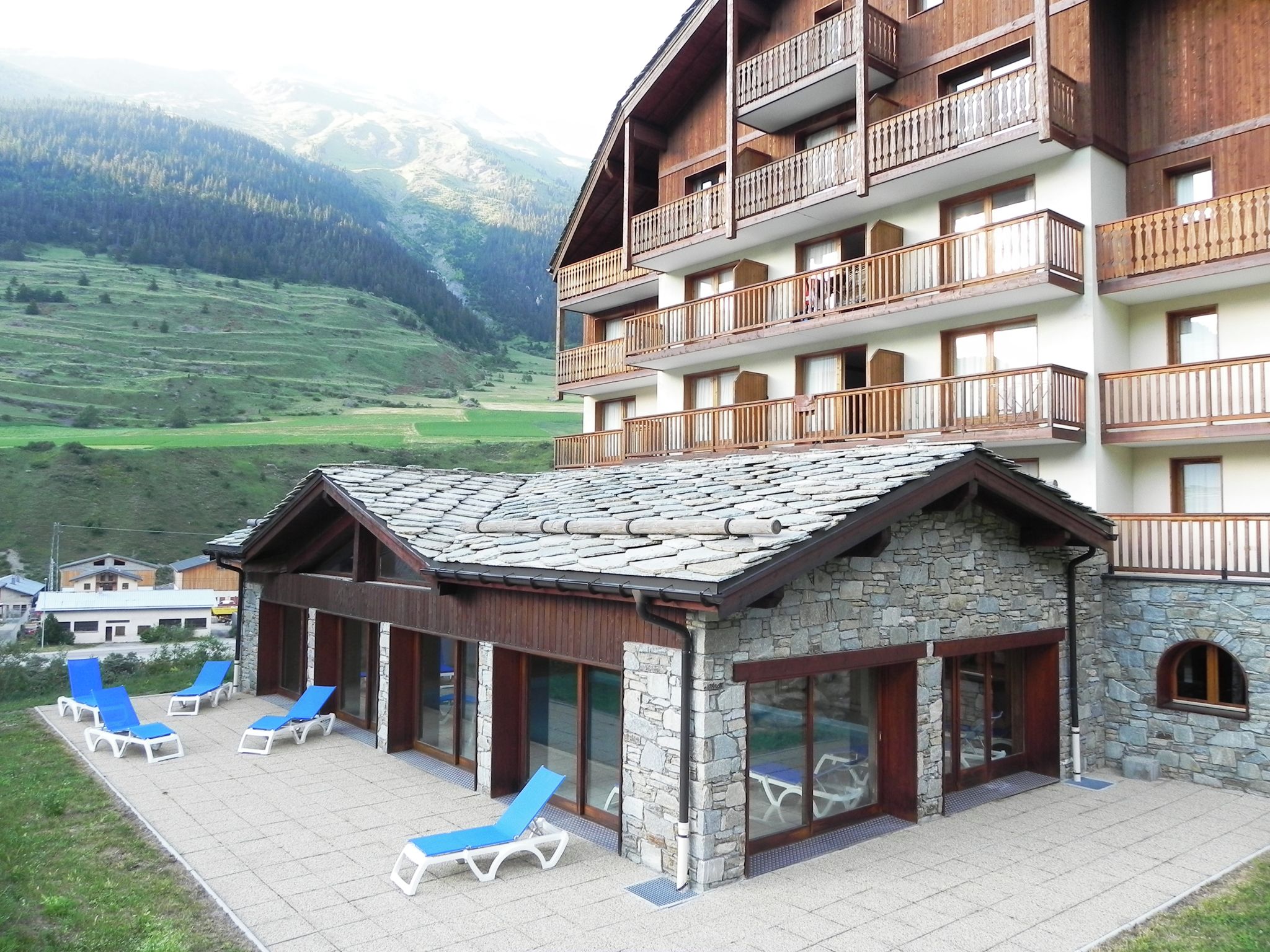 A mountain lodge with a stone facade, wooden balconies, and a patio with sun loungers.