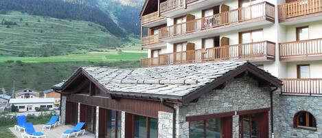 A mountain lodge with a stone facade, wooden balconies, and a patio with sun loungers.