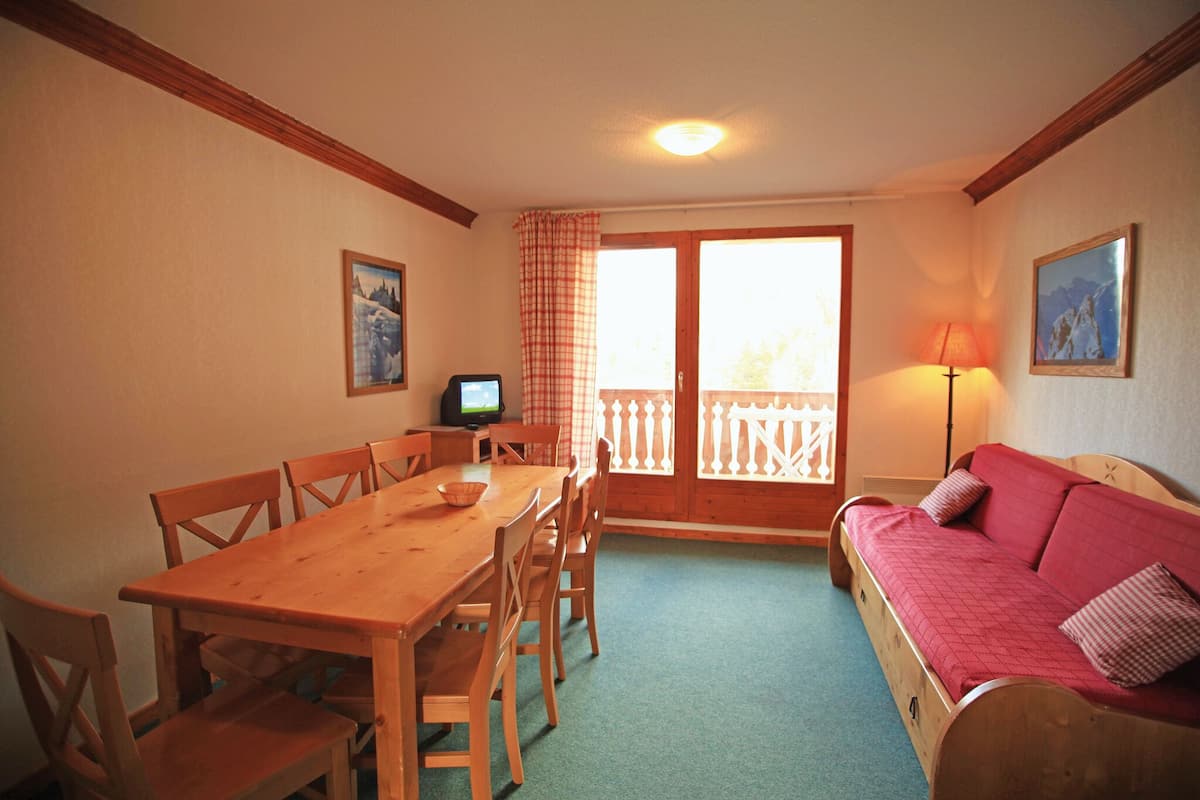 Une pièce chaleureuse avec une table à manger en bois, des chaises, un canapé rouge et un téléviseur posé sur une petite table.