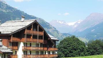 A wooden chalet with multiple balconies, set against a backdrop of mountains and clear skies.
