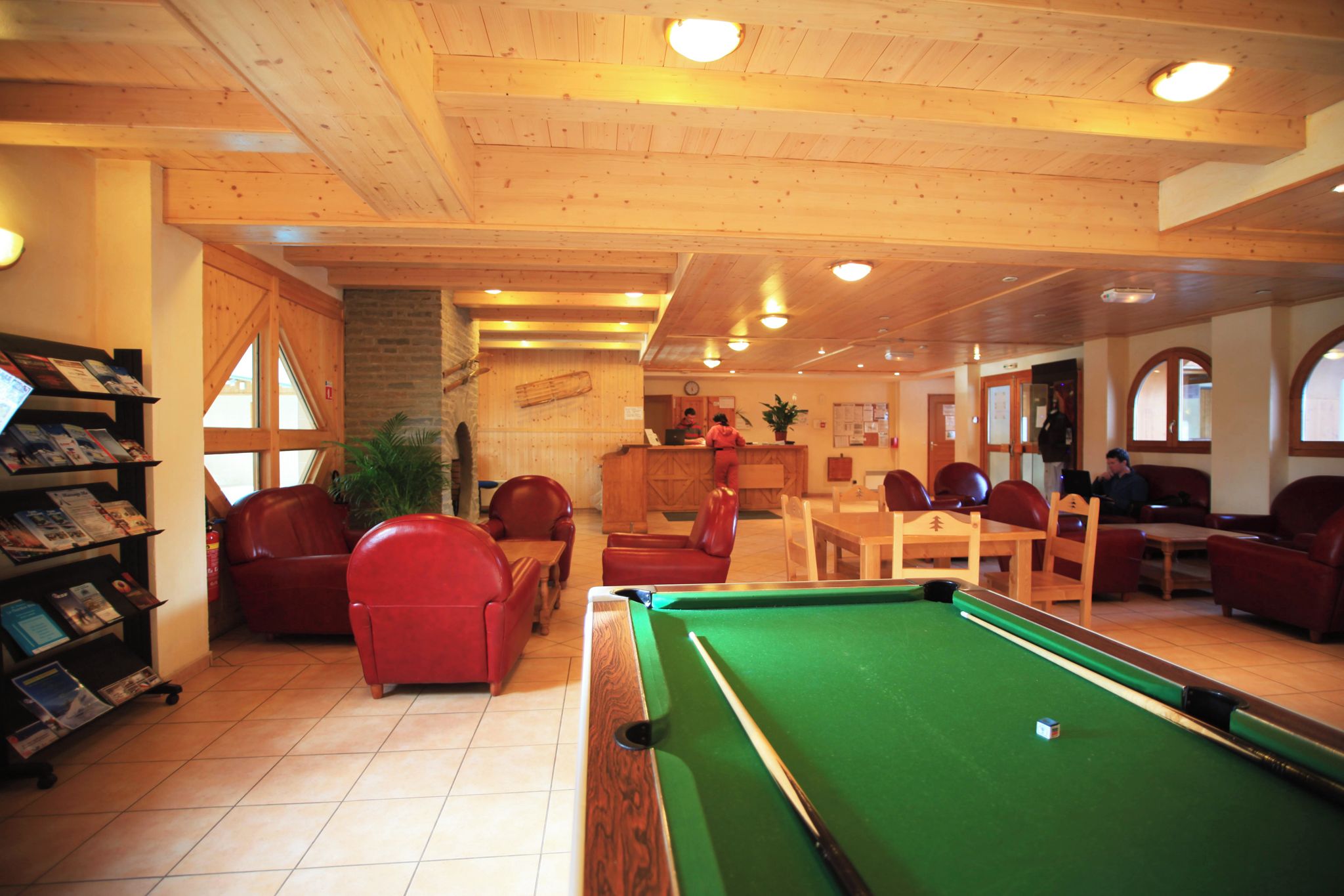 A pool table with red chairs, a wooden ceiling, and a brick wall.