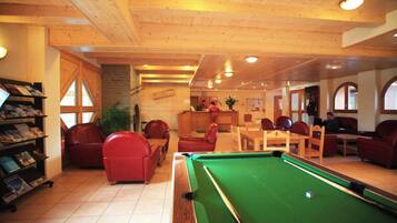 A pool table with red chairs, a wooden ceiling, and a brick wall.