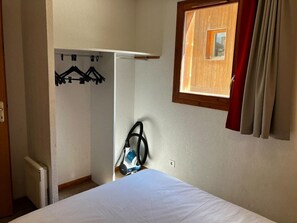 Un dormitorio con cama, aspiradora, perchero y ventana con cortinas.