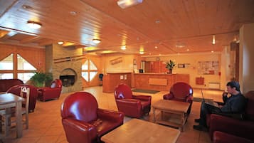 A cozy interior with wooden ceilings, red leather chairs, a fireplace, a reception desk, and a laptop on a table.