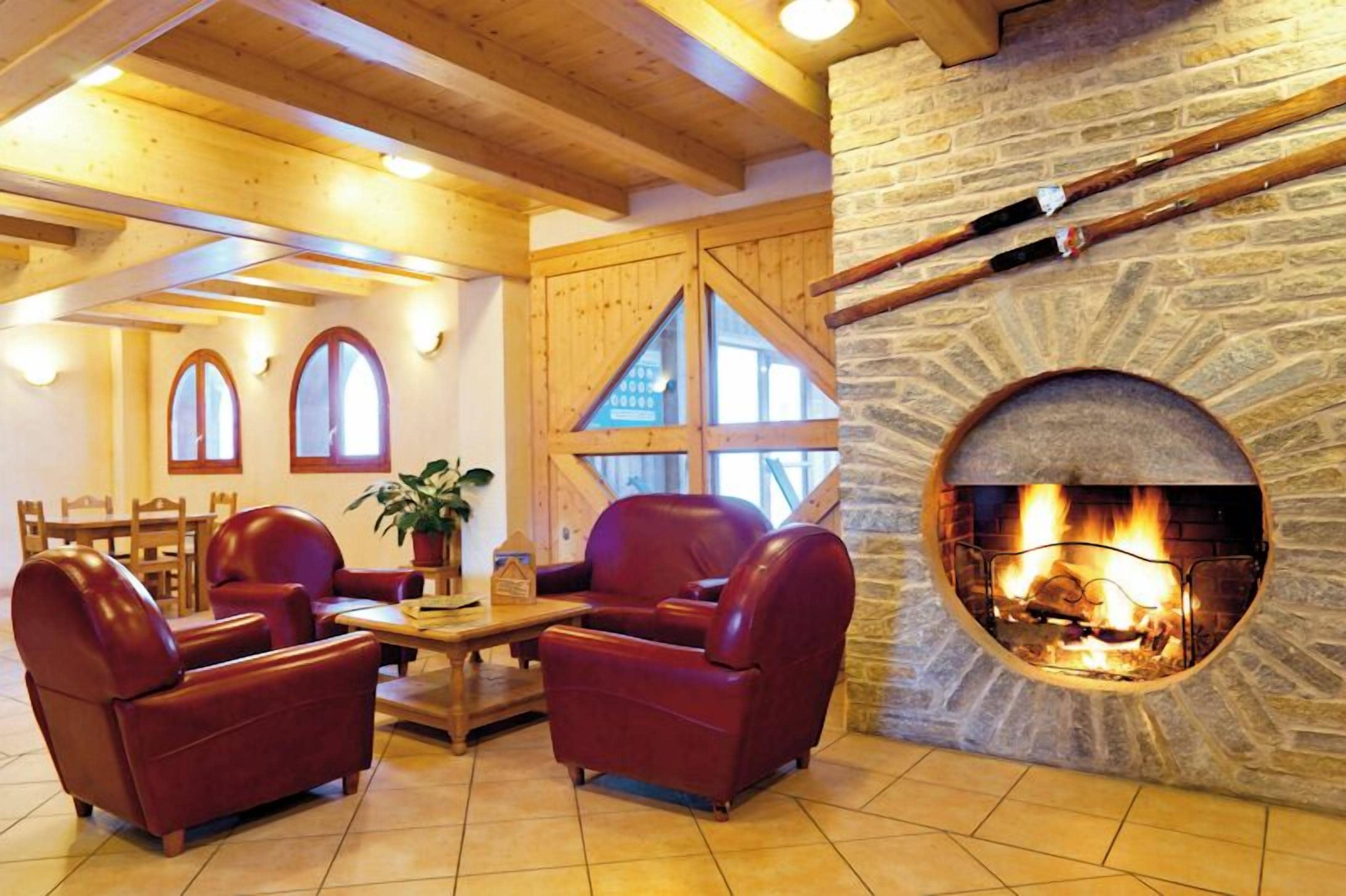 A cozy room with a stone fireplace, leather sofas, wooden beams, and a dining area with a table and chairs.