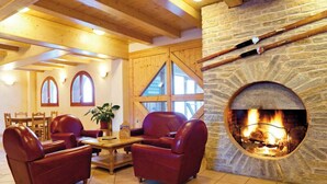 A cozy room with a stone fireplace, leather sofas, wooden beams, and a dining area with a table and chairs. - Lagrange Vacances Les Valmonts De Val Cenis (Val-Cenis)