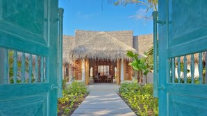 A pathway leading to a building with a thatched roof and a dining area. - Milaidhoo Island Maldives (Milaidhoo Island)