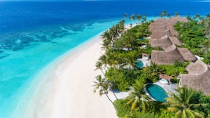 An aerial view of a beach resort with thatched-roof villas, a swimming pool, and a clear turquoise sea. - Milaidhoo Island Maldives (Milaidhoo Island)