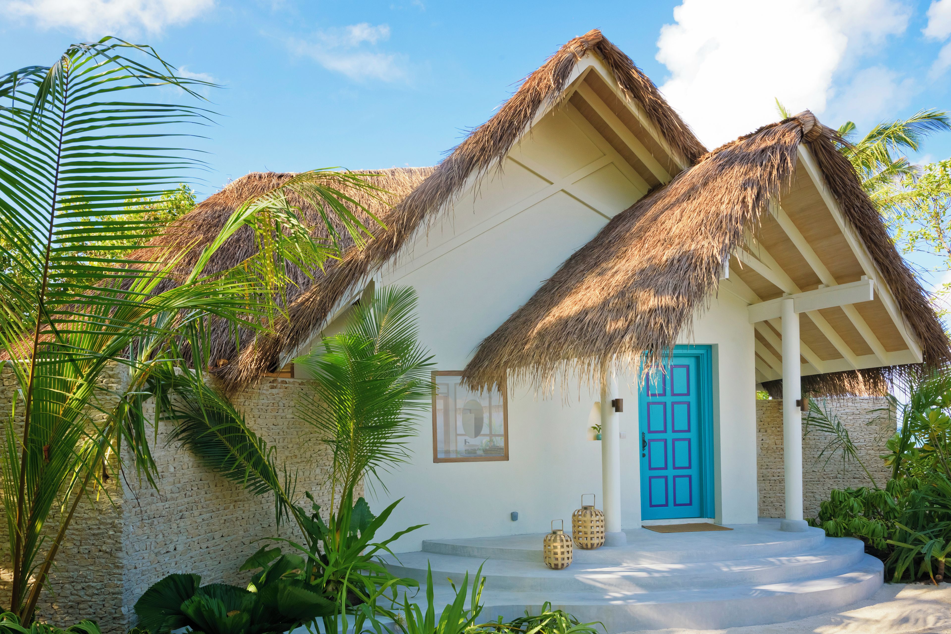 A thatched-roof house with a blue door, surrounded by lush greenery.