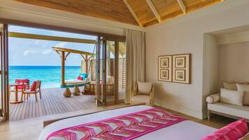A hotel room with a large bed, a view of the ocean, a balcony with a table and chairs, and a wooden ceiling.