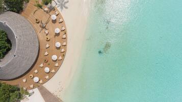 An aerial view of a beach resort with a circular wooden deck, lounge chairs, and umbrellas.