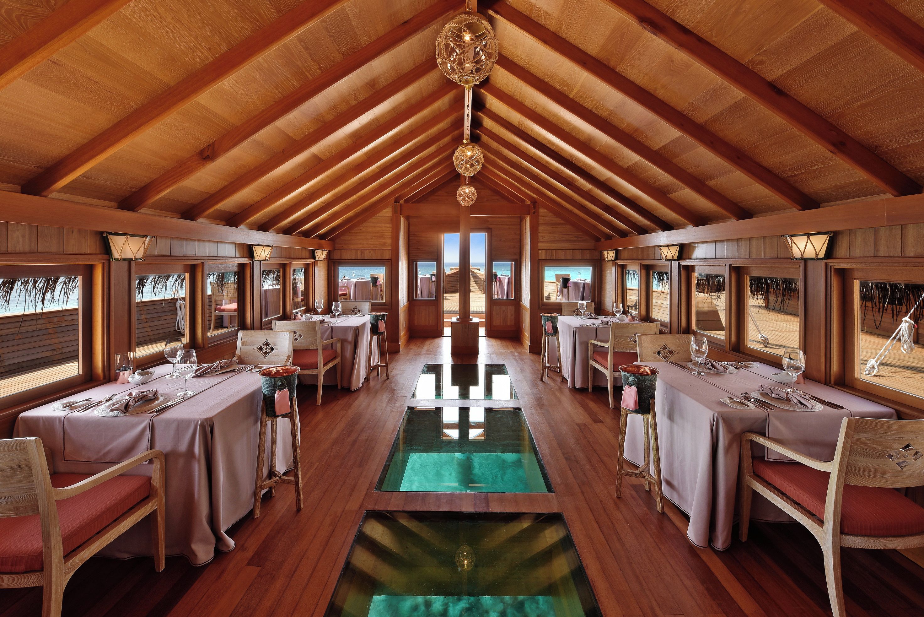 A restaurant with wooden beams, tables set for dining, and a view through the windows.