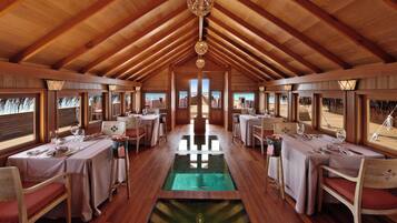 A restaurant with wooden beams, tables set for dining, and a view through the windows.
