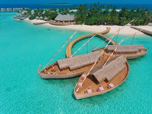 Um resort tropical com bangalôs sobre a água, águas turquesa cristalinas e palmeiras.