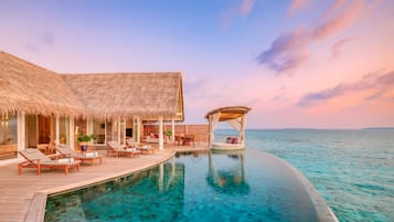 An infinity pool with a wooden deck, lounge chairs, and a cabana.