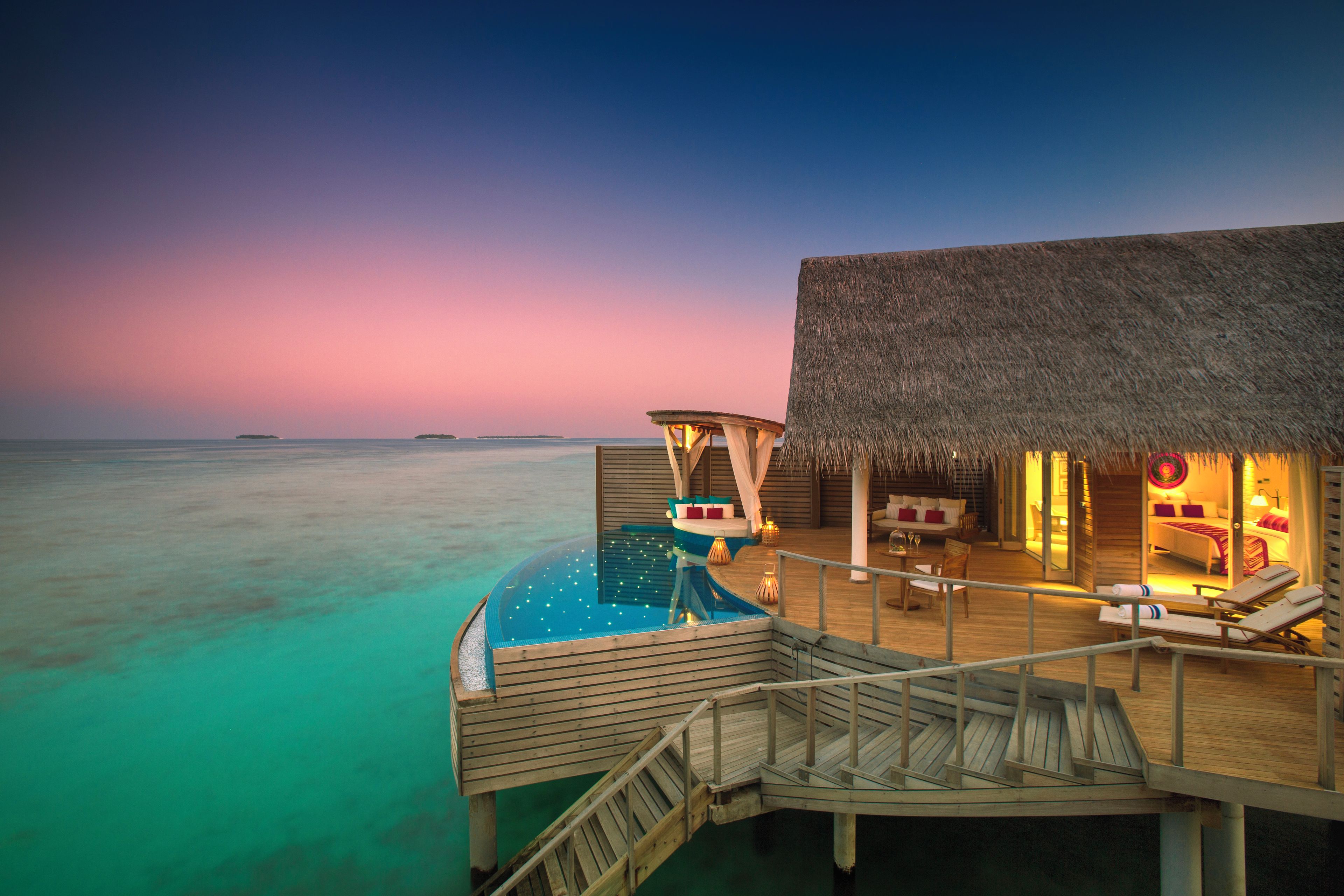 A resort overwater bungalow with a private pool, wooden deck, and thatched-roof lounge area.
