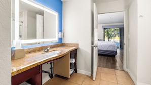 A bathroom with a marble sink, a large mirror, and a door leading to a bedroom. - Spacious Accessible 2BR Suite | King + 2 Queens | Santa Cruz (Santa Cruz)