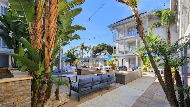 A poolside area with seating, palm trees, and a building with balconies. - Spacious Accessible 2BR Suite | King + 2 Queens | Santa Cruz (Santa Cruz)