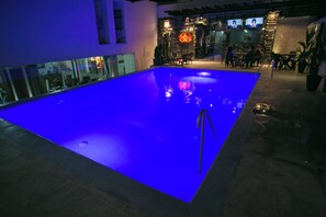 An indoor swimming pool with a blue-lit water feature, a bar area with seating, and a neon sign. - Hotel D' Leon (Floridablanca)
