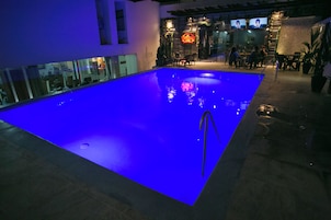 Una piscina interior con una fuente iluminada en azul, una zona de bar con asientos y un letrero de neón.