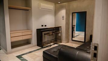 Ein modernes Zimmer mit einer schwarzen Ledersofa, einem Holztisch mit zwei Stühlen, einer eingebauten Klimaanlage und einem großen Spiegel, der eine blaue Wand reflektiert.