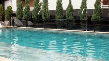 Ein rechteckiger Pool mit klarem Wasser, umgeben von einem schwarzen Zaun und hohen, schmalen Bäumen.