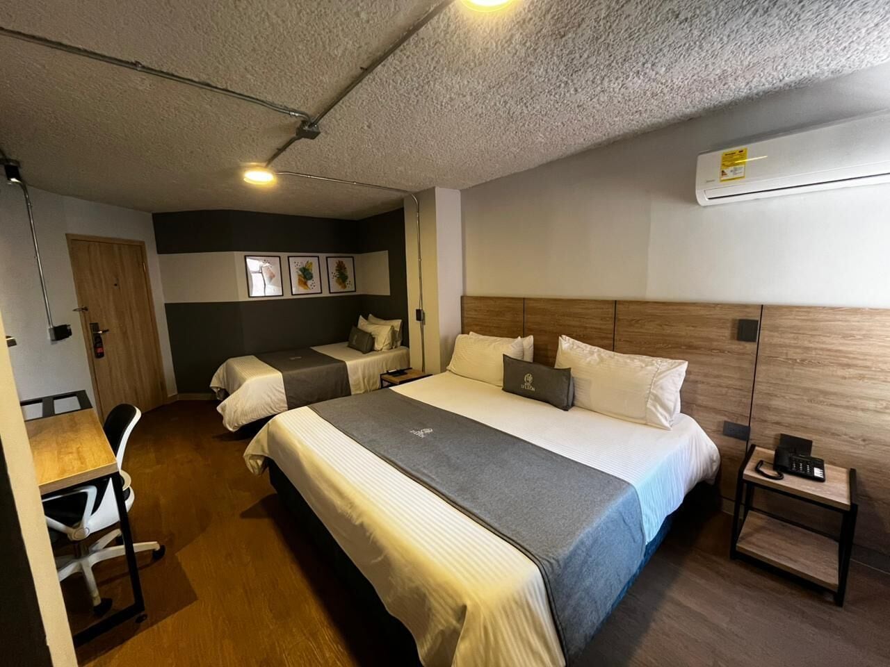 Ein Hotelzimmer mit einem großen Bett, einem Schreibtisch, einem Sessel, einem Nachttisch mit Telefon und einer wandmontierten Klimaanlage.