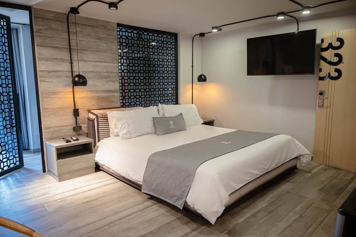 Quarto moderno com cama, mesas de cabeceira, televisão e um painel decorativo na parede.