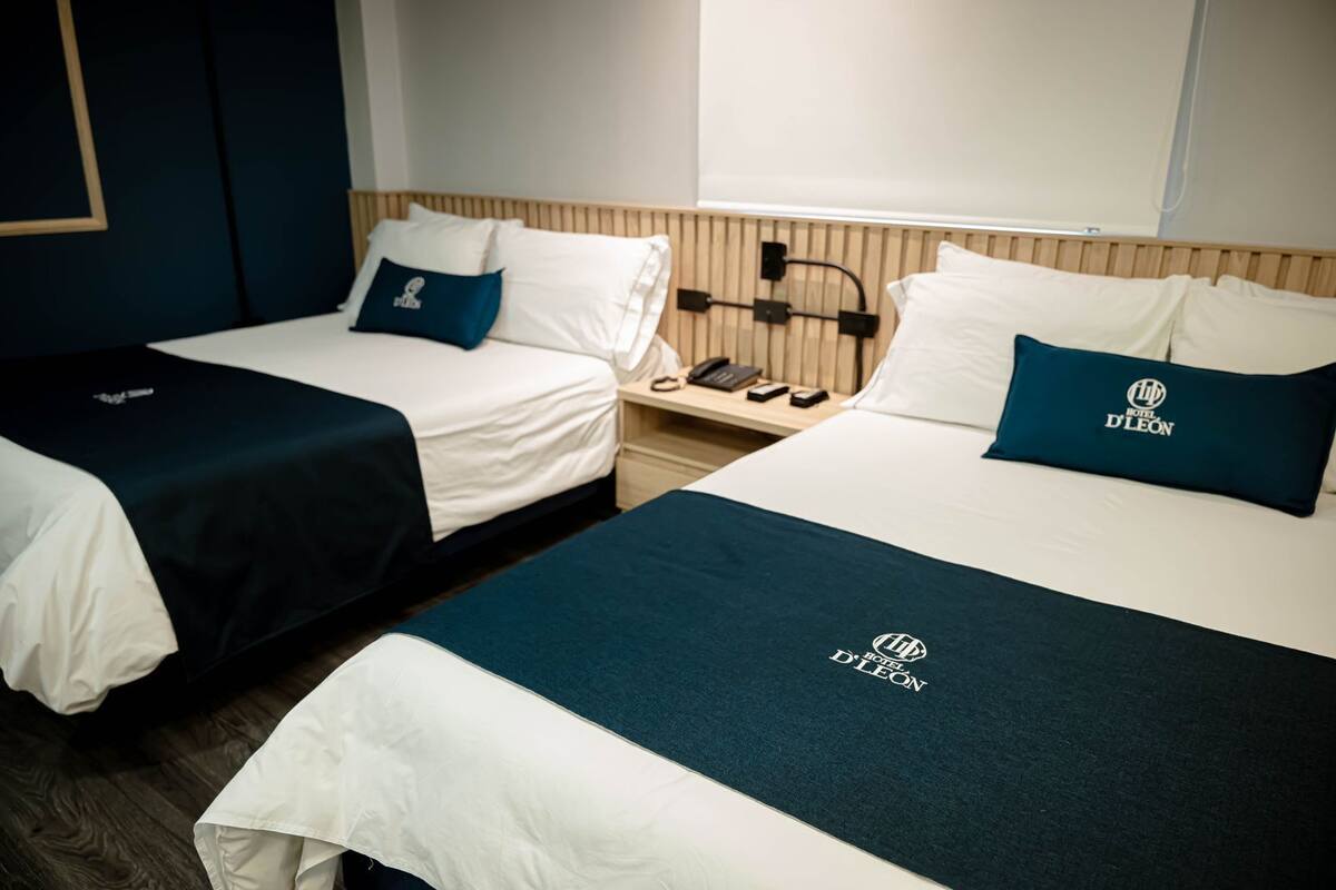 Duas camas de solteiro com roupa de cama branca e cabeceiras azul escuras, uma mesa de cabeceira com um telefone e uma luminária, e uma cabeceira de madeira.