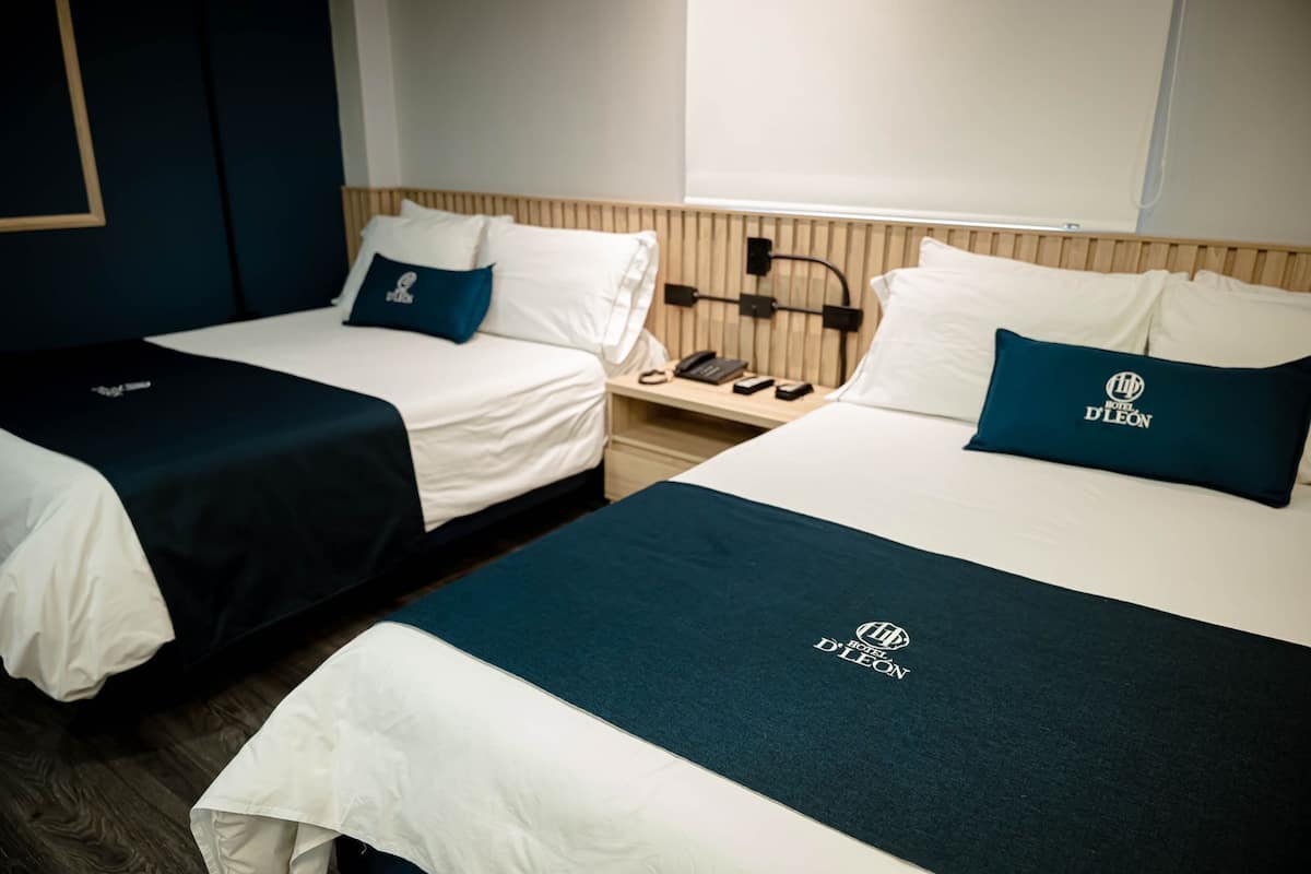 Zwei Einzelbetten mit weißer Bettwäsche und dunkelblauen Kopfteilen, ein Nachttisch mit Telefon und Lampe sowie ein Holz-Kopfteil.