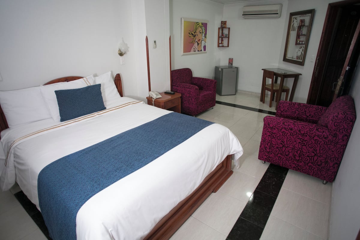 Quarto de hotel com uma cama grande, uma escrivaninha, uma cadeira e um frigorífico.